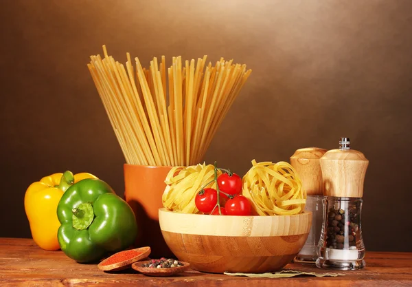 Spaghetti, tagliatelle in ciotola, pomodorini alla paprica ciliegia su tavolo di legno su fondo marrone — Foto Stock