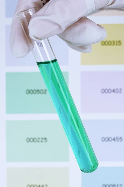 Tubo con líquido azul en la mano sobre el fondo de muestras de color — Foto de Stock
