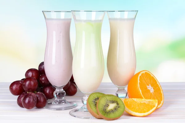 Batidos de leche con frutas sobre la mesa sobre fondo azul claro —  Fotos de Stock