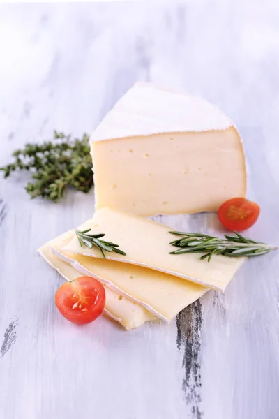 Tasty Camembert cheese with tomato and rosemary, on wooden table — Stock Photo, Image