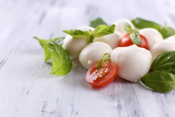 Tasty mozzarella cheese with basil and tomatoes, on wooden table — Stock Photo, Image