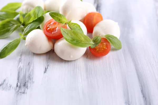 Tasty mozzarella cheese with basil and tomatoes, on wooden table — Stock Photo, Image