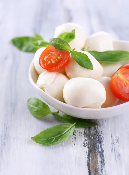 Tasty mozzarella cheese with basil and tomatoes in bowl, on wooden table — Stock Photo, Image