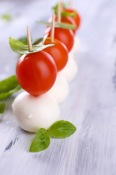 Tasty mozzarella cheese with basil and tomatoes, on wooden table — Stock Photo, Image