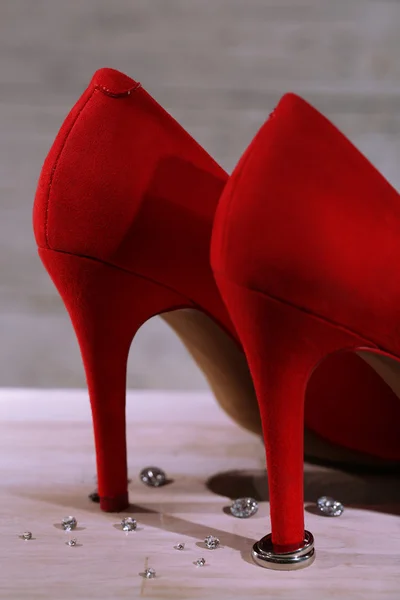 Hermosos anillos de boda en el talón del zapato femenino rojo, sobre fondo de madera — Foto de Stock