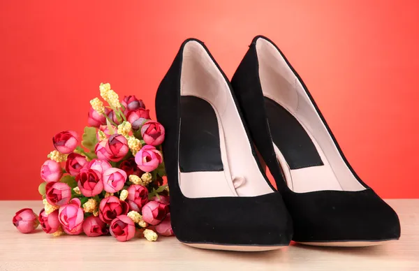 Krásné černé ženské boty a květiny na červeném pozadí — Stock fotografie