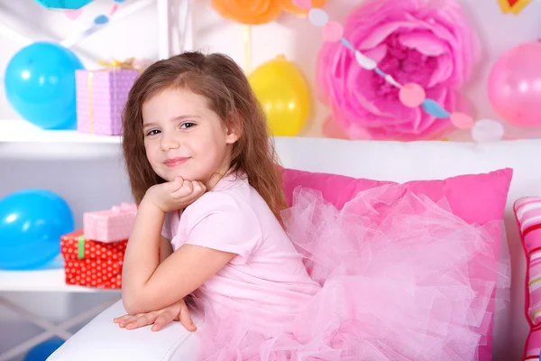 Pretty little girl sitting on sofa on celebratory background — Stock Photo, Image