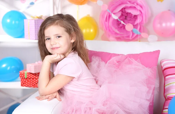 Pretty little girl sitting on sofa on celebratory background — Stock Photo, Image