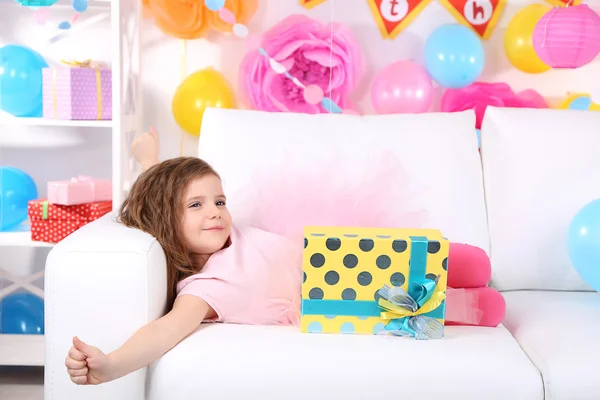 Küçük tatlı kız kutlama arka plan üzerinde kanepe üzerinde kaymasını — Stok fotoğraf