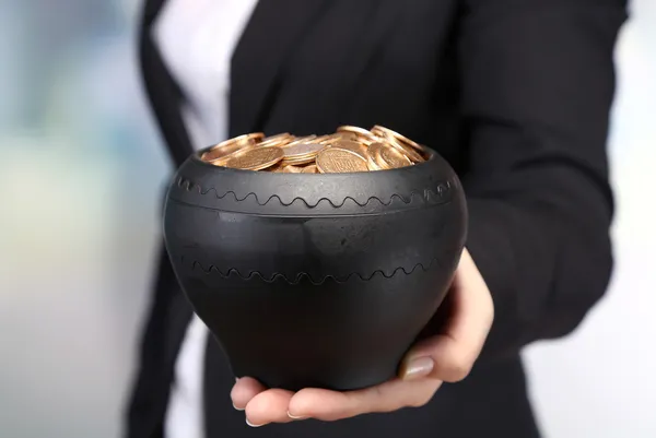 Keramische pot met gouden munten in vrouwelijke handen, op lichte achtergrond — Stockfoto