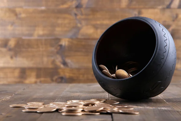 Golden coins falling out from pot, on wooden background — Stock Photo, Image