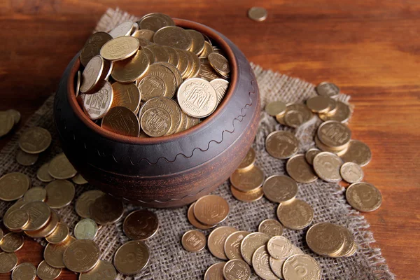 Gouden munten in keramische pot, op houten achtergrond — Stockfoto