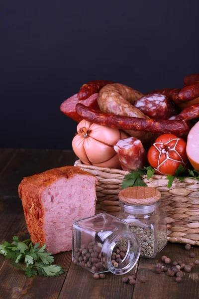 Lot of different sausages in basket on wooden table on black background — Stock Photo, Image