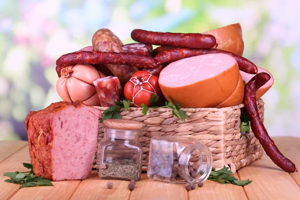 Lot of different sausages in basket on wooden table on natural background — Stock Photo, Image