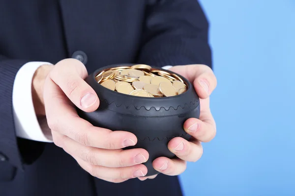 Ceramic pot with golden coins in male hands, on color background — Stock Photo, Image