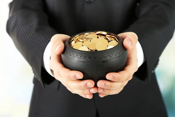 Maceta de cerámica con monedas de oro en manos masculinas, sobre fondo claro — Foto de Stock