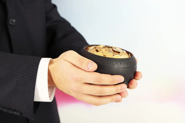 Pot en céramique avec des pièces d'or dans les mains des hommes, sur fond clair — Photo