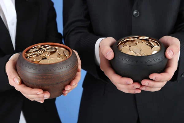 Two ceramic pots with golden coins in male and female hands, on color background — Stock Photo, Image