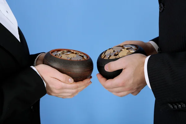 Dos ollas de cerámica con monedas de oro en manos masculinas y femeninas, sobre fondo de color — Foto de Stock