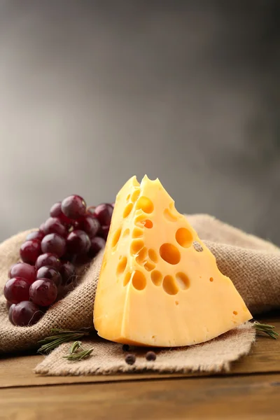 Кусок сыра с виноградом и розмарином на деревянном столе, на темном фоне — стоковое фото