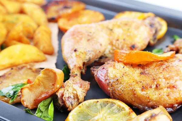 Homemade roasted chicken drumsticks with fried potatoes and vegetables on pan, close-up — Stock Photo, Image