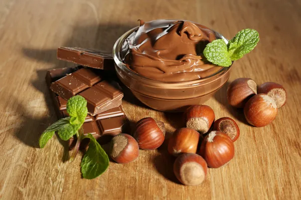 Söt choklad hasselnöt sprida med hela nötter och mynta på trä bakgrund — Stockfoto