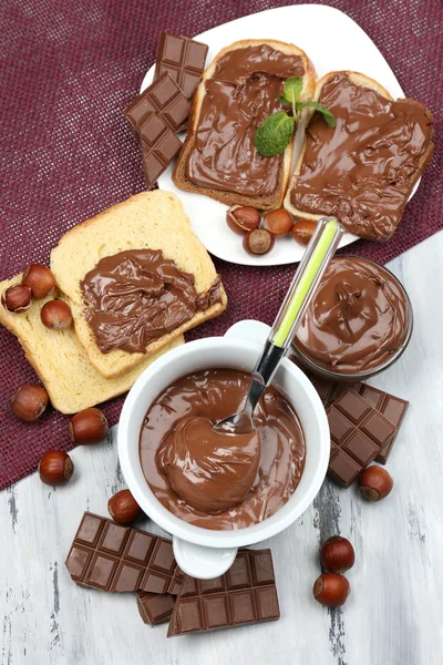 Zoete chocolade hazelnoot verspreid met hele noten en munt op houten achtergrond — Stockfoto