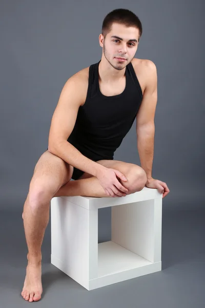 Guapo joven sentado en cubo sobre fondo gris —  Fotos de Stock