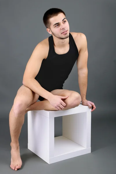 Guapo joven sentado en cubo sobre fondo gris —  Fotos de Stock