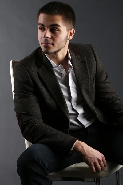 Handsome young sitting on chair on dark background — Stock Photo, Image