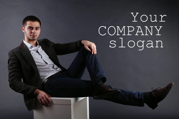 Handsome young sitting on cube on dark background — Stock Photo, Image