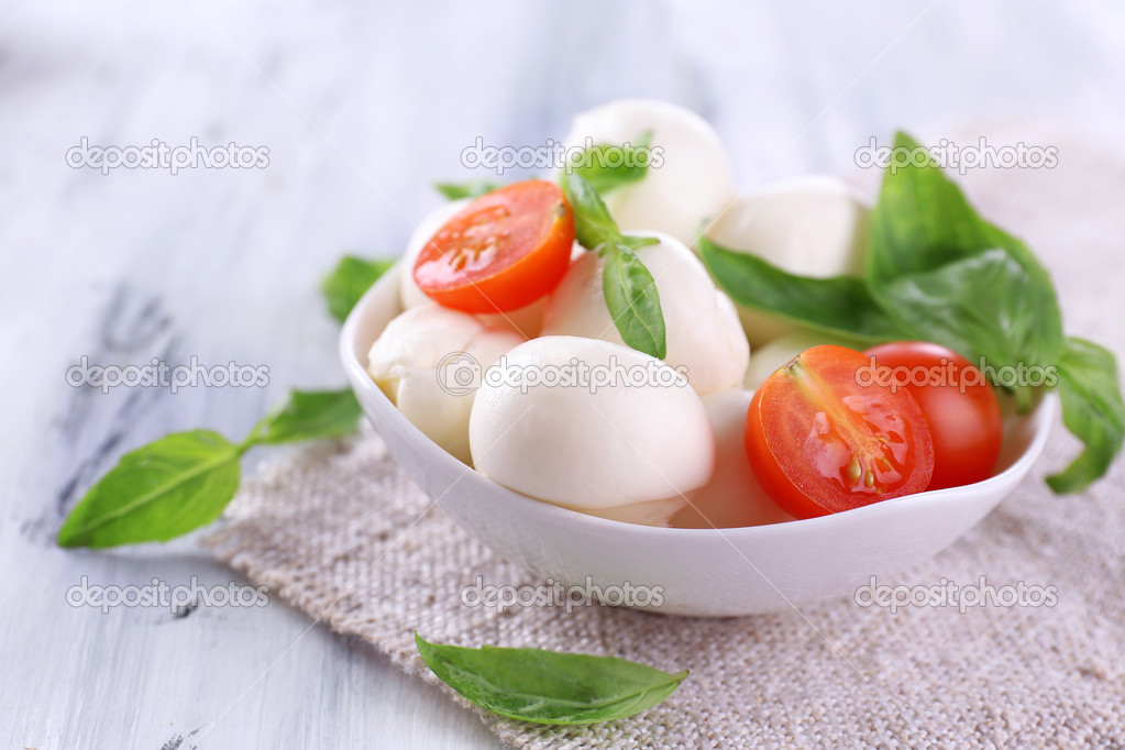 Tasty mozzarella cheese with basil and tomatoes in bowl, on wooden table