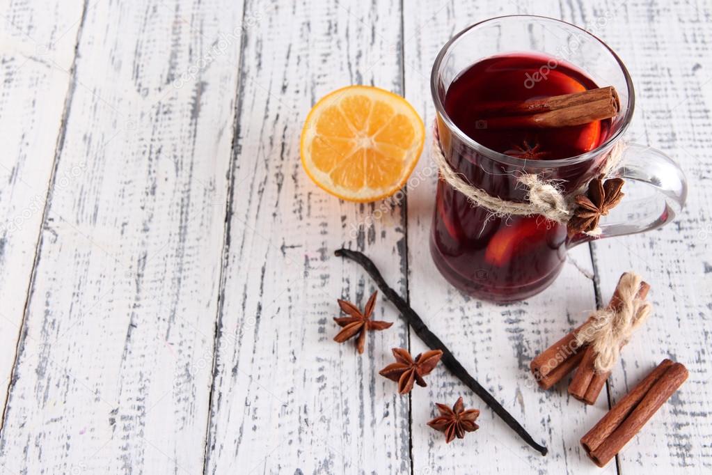 Mulled wine with lemon and spices on wooden background