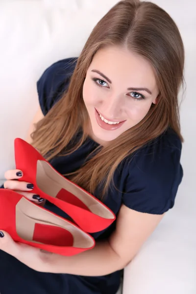 Девушка сидит на диване в сексуальной красной обуви, на домашнем фоне интерьера — стоковое фото