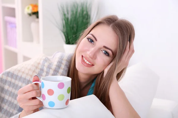 Jeune femme au repos avec une tasse de boisson chaude sur le canapé à la maison — Photo