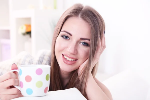 Junge Frau ruht mit Tasse Heißgetränk auf Sofa zu Hause — Stockfoto