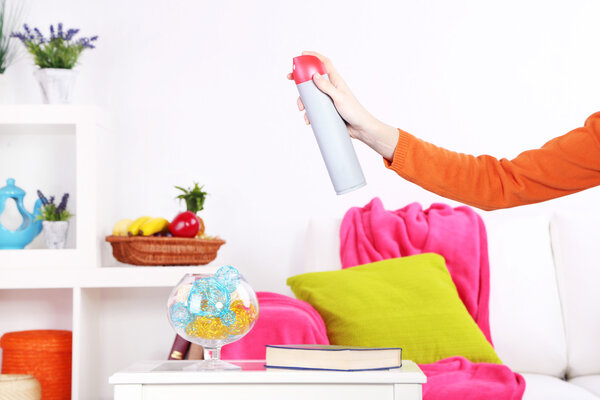 Sprayed air freshener in hand on home interior background