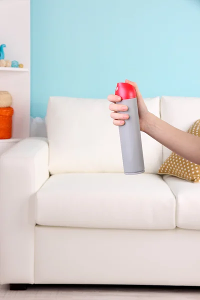 Sprayed air freshener in hand on sofa background — Stock Photo, Image