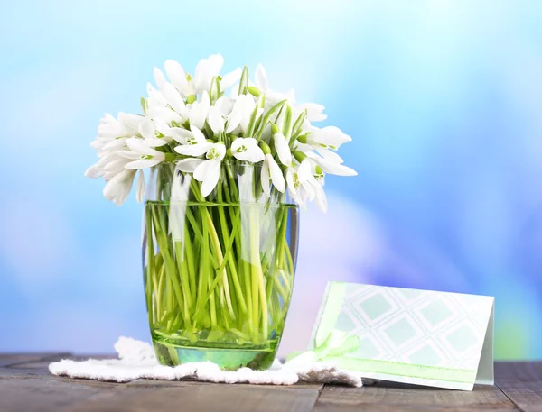 Beautiful snowdrops in vase, on wooden table on bright background — Stock Photo, Image