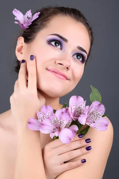 Hermosa joven con flores sobre fondo gris — Foto de Stock