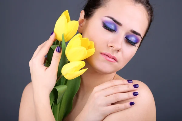 Schöne junge Frau mit Blumen auf grauem Hintergrund — Stockfoto