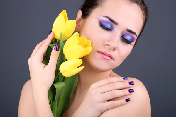 Bella giovane donna con fiori su sfondo grigio — Foto Stock