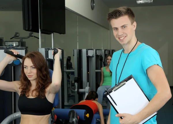 Fille et entraîneur engagés dans le simulateur dans la salle de gym — Photo