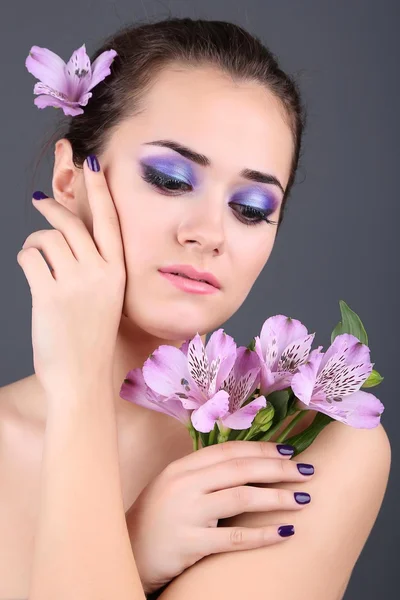 Hermosa joven con flores sobre fondo gris — Foto de Stock