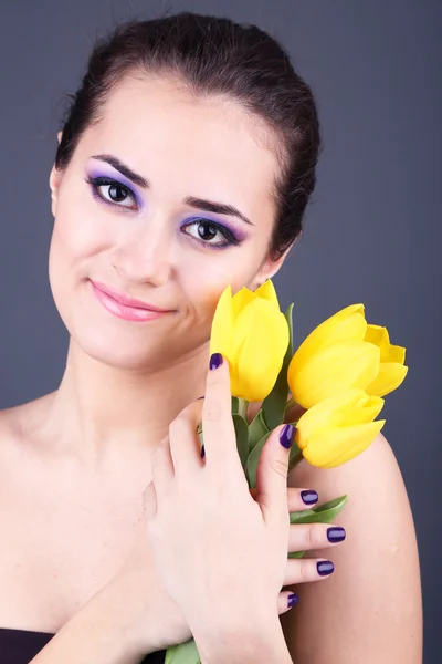 Wanita muda cantik dengan bunga di latar belakang abu-abu — Stok Foto