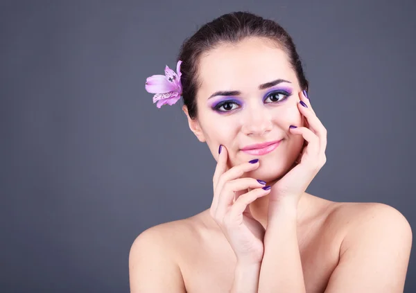 Mulher bonita com flor no cabelo no fundo cinza — Fotografia de Stock