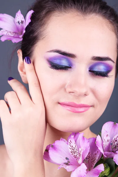 Schöne junge Frau mit Blumen auf grauem Hintergrund — Stockfoto