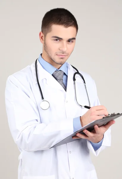 Mannelijke arts permanent met map, op een grijze achtergrond — Stockfoto