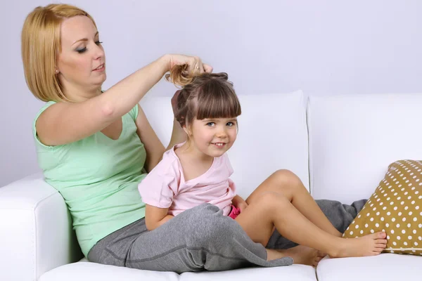 Hübsches kleines Mädchen sitzt mit Mutter auf Sofa auf grauem Hintergrund — Stockfoto