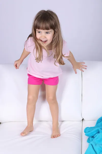 Pretty little girl jumping on sofa on gray background — Stock Photo, Image